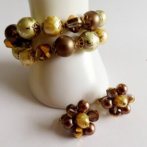 May include: A set of vintage jewelry featuring a bracelet and a pair of clip-on earrings. The bracelet has large, round beads in shades of gold and brown. The earrings have a cluster design with similar colors and textures.