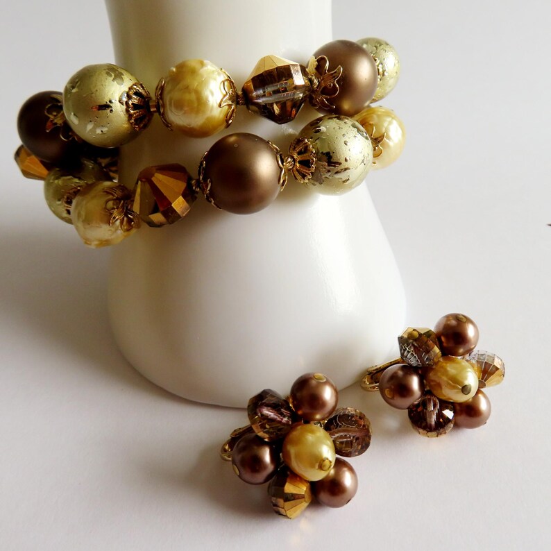 May include: A set of vintage jewelry featuring a bracelet and a pair of clip-on earrings. The bracelet has large, round beads in shades of gold and brown. The earrings have a cluster design with similar colors and textures.
