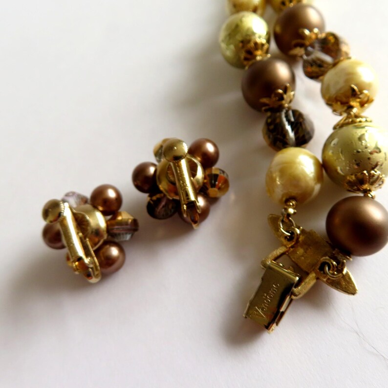 May include: Vintage jewelry set featuring a necklace and clip-on earrings. The necklace has a strand of brown, gold, and clear beads. The earrings are clusters of brown beads with gold-tone metal clips. The necklace clasp is gold-toned and marked "Vendome".