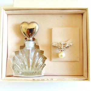 May include: A vintage gift set in a cream-colored box. It includes a clear glass perfume bottle with a silver heart-shaped stopper and a rhinestone and pearl brooch. The box has the text "Especially for You" and "Roman".