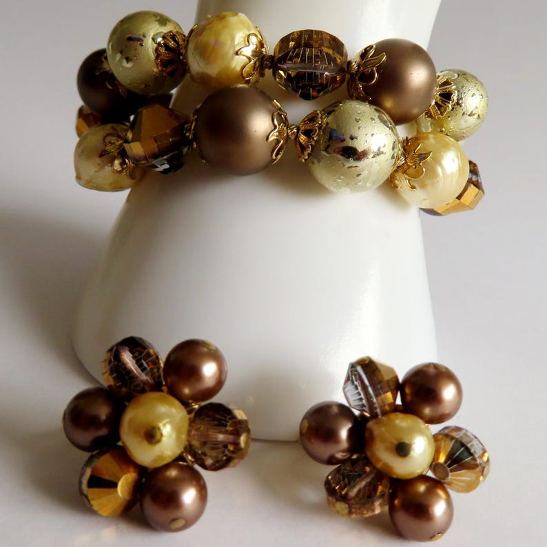 May include: A vintage jewelry set featuring a bracelet and matching earrings. The bracelet is composed of large, round beads in shades of gold, brown, and cream. The earrings have a cluster design with similar beads. The jewelry is displayed on a white surface.