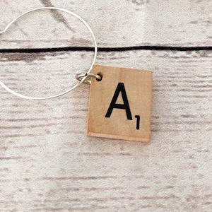 May include: A single silver hoop earring with a wooden tile charm. The charm is a square tile with the letter "A" and the number "1" printed in black. The earring is shown against a light wood grain background.