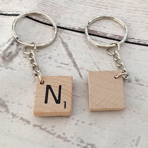 May include: Two keychains featuring square light-colored wooden tiles attached to silver-toned metal split rings by short chains. One tile displays the black letter N with the number 1, while the other tile is blank and shows a natural wood grain.