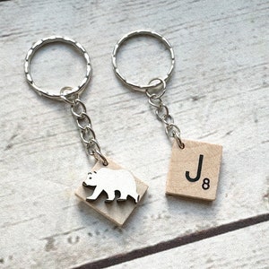 May include: Two keychains with silver key rings and chains. One keychain has a wooden tile with the letter J and the number 8. The other keychain has a wooden tile with a white silhouette of a bear.
