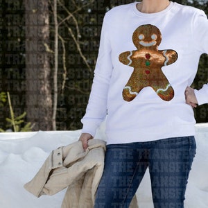 May include: White sweatshirt with a gingerbread man design made of sequins. The gingerbread man is brown with red and green accents.