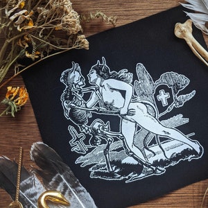May include: Black fabric patch with a white design of a woman with horns and a skeleton. The woman is holding the skeleton's hand and they are both standing on a cross. The design is surrounded by a cloud with a cross in it.