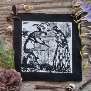 Puede incluir: Ilustración en blanco y negro de una mujer con un vestido largo hablando con una criatura parecida a una cabra con cuernos. La imagen está impresa en un parche de tela negro.