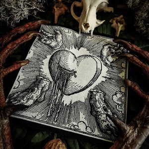 May include: A monochrome illustration of a heart with radiating lines and cloud motifs on a white square. The image is set against a dark backdrop with a skull, bird claws, and other natural elements. The style is reminiscent of vintage woodcuts.