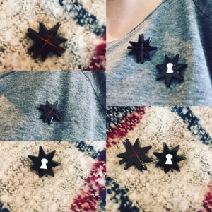 May include: Four black star-shaped pins with a red line across the center. Two of the pins have a white keyhole shape in the center.