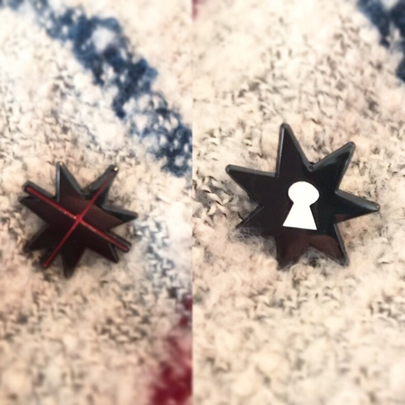 May include: Two black star-shaped pins with a red cross on one and a white keyhole on the other.