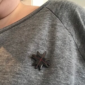 May include: A gray long-sleeved shirt with a black star-shaped pin with a red cross in the center.