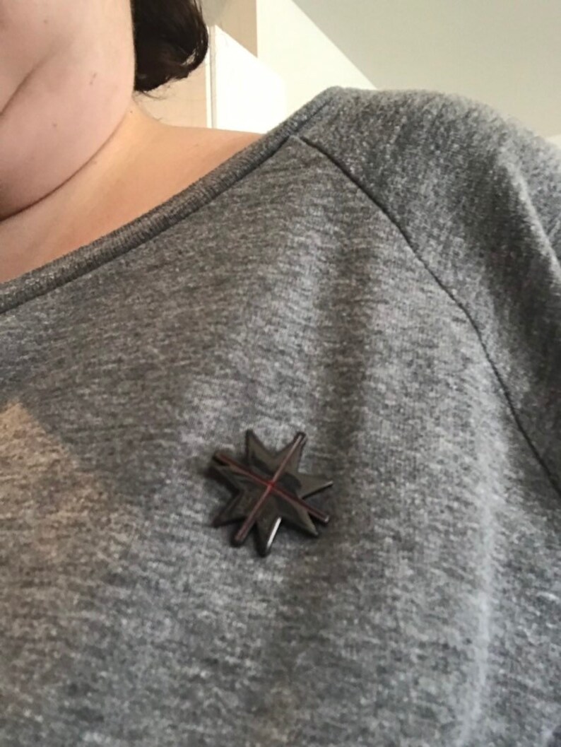 May include: A gray long-sleeved shirt with a black star-shaped pin with a red cross in the center.