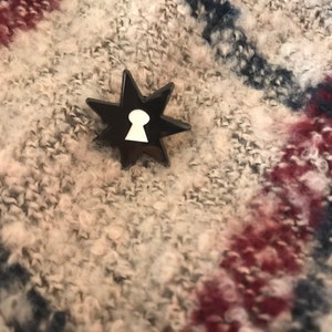 May include: A black star-shaped pin with a white keyhole design in the center.