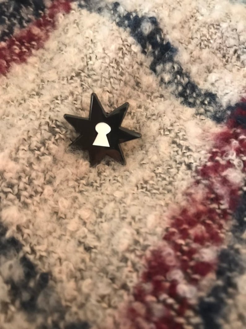 May include: A black star-shaped pin with a white keyhole design in the center.