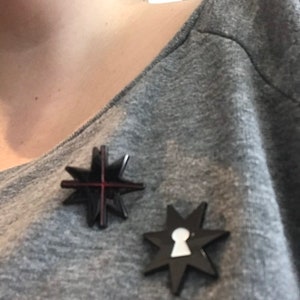 May include: Two black star-shaped pins with a red cross and a white keyhole design.