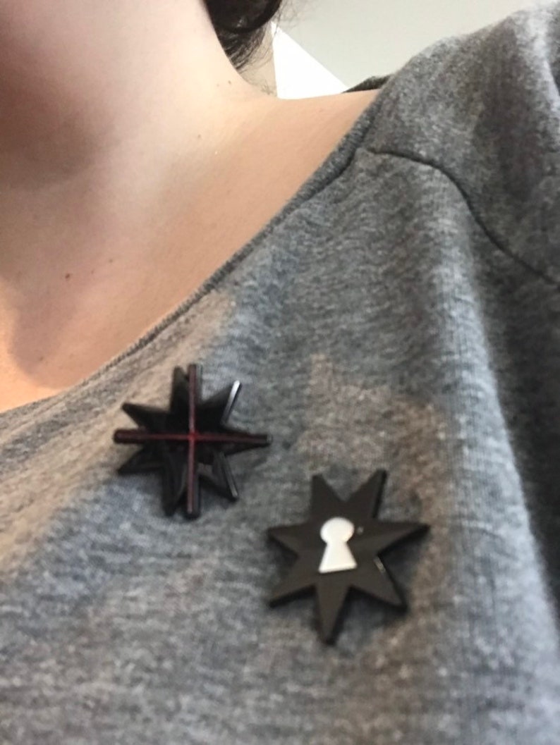 May include: Two black star-shaped pins with a red cross and a white keyhole design.