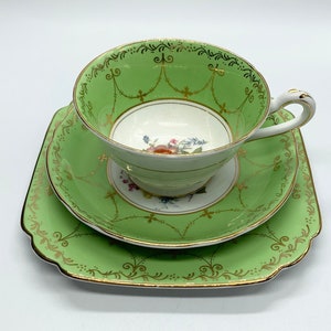 May include: A vintage tea set featuring a green teacup, saucer, and square plate. The set has gold trim and decorative patterns. The teacup and saucer have a floral design in the center.