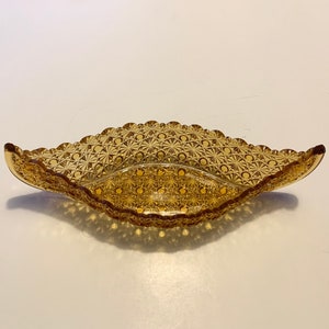 May include: Amber-colored, oval-shaped glass dish with a scalloped edge. The dish features a detailed, repeating pattern of small circles and lines. The decorative bowl is likely vintage and suitable for serving or display.