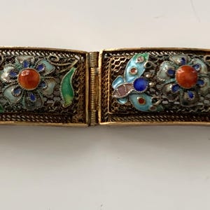May include: A vintage gold-coloured bracelet with rectangular links. Each link has a filigree design with a central flower and butterfly motifs, accented with turquoise, blue, red, and green enamel details. A piece of antique jewellery.