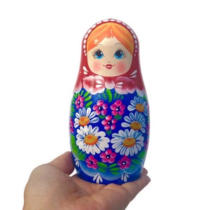 May include: A traditional Russian nesting doll, also known as a matryoshka doll, painted with a colorful floral pattern. The doll is wearing a red headscarf and has a smiling face.