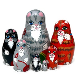 Puede incluir: Un conjunto de seis muñecas rusas, o muñecas matrioska, con motivos de gatos. La muñeca más grande es gris con la cara blanca y las orejas rosas. La segunda muñeca más grande es naranja con la cara blanca y las patas blancas. Las muñecas restantes son más pequeñas y presentan una variedad de colores y diseños.