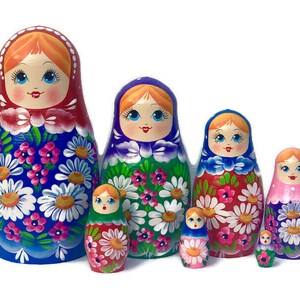 May include: A set of seven traditional Russian nesting dolls, or matryoshka dolls. The dolls are painted with colorful floral patterns and have smiling faces. The largest doll is blue with white flowers, the next is green with white flowers, the next is red with white flowers, the next is pink with white flowers, and the smallest three dolls are red, blue, and green.