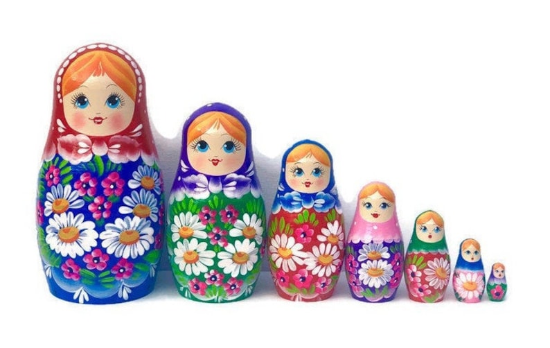 May include: A set of eight traditional Russian nesting dolls, also known as matryoshka dolls. The dolls are painted with colorful floral patterns and feature smiling faces. The largest doll is blue with red, white, and pink flowers. The dolls decrease in size, with the smallest doll being a miniature version of the largest.