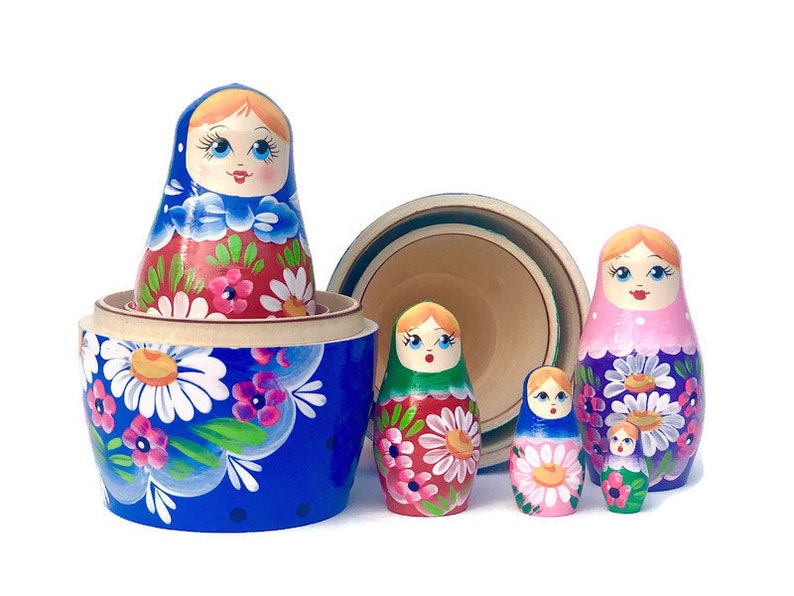 May include: A set of five traditional Russian nesting dolls, or matryoshka dolls. The largest doll is blue with white flowers and is open to reveal a smaller doll inside. The other dolls are painted in various colors with floral designs.