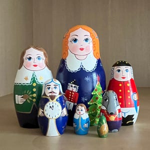 May include: A set of eight traditional Russian nesting dolls, or matryoshka dolls, painted with a Christmas theme. The largest doll is a woman with red hair wearing a blue dress. The other dolls depict a man in a green jacket, a man with a beard and a compass, a woman in a blue dress, a man in a red coat, a gray wolf, and two smaller dolls.