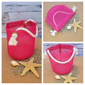 May include: Three pink mesh bags with white rope handles. The bags are on a sandy surface with seashells and starfish.