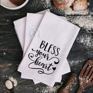 May include: Set of three white kitchen towels with black text that reads "Bless your heart" with a crescent moon and heart design.