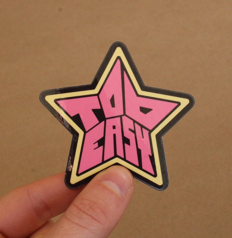 May include: A pink and black star-shaped sticker with the text "Too Easy" inside.