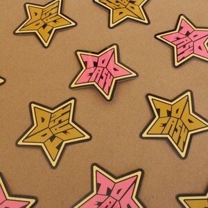 May include: A set of ten star-shaped stickers with the words "Too Easy" printed on them. The stickers are in two colors: pink and yellow.