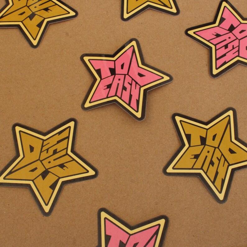 May include: A set of six star-shaped stickers with the text "Too Easy" in a retro font. The stickers are in two colors: pink and gold.