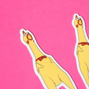 May include: Two yellow rubber chicken stickers with red bows on a pink background. The chickens are looking up with their mouths open.