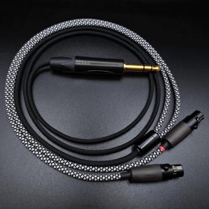 Pode incluir: Um cabo trançado preto e branco com um conector TRS de 1/4 de polegada banhado a ouro em uma extremidade e dois conectores TRS de 3,5 mm pretos e prateados na outra extremidade.