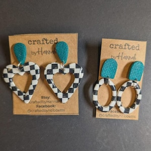 May include: Two pairs of handmade earrings. One pair features heart-shaped pendants with a black and white checkerboard pattern, and the other pair has oval-shaped pendants with the same pattern. Both pairs have teal-colored top accents.