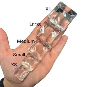 以下が含まれることがあります： XS、Small、Medium、Large、XLとラベルされた、さまざまなサイズの5つの正方形の容器を備えた透明なガラス製品。容器は白い背景に対して手で持たれています。この製品は、測定ツールまたは保管ソリューションのようです。