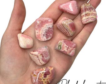 May include: A collection of eight polished rhodochrosite stones with varying shades of pink, white, and cream. Each stone features unique banded patterns and a smooth, glossy finish. The stones are displayed together, showcasing their natural mineral textures.