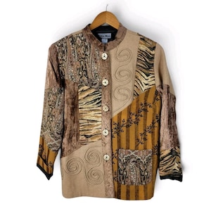 Könnte beinhalten: Eine langärmelige Jacke mit Patchwork-Design aus verschiedenen braunen, beigen und goldenen Stofftexturen, darunter Paisley-, Tierfell- und Streifenmuster. Die Jacke hat einen Stehkragen, fünf helle Knöpfe und eine aufgesetzte Tasche.