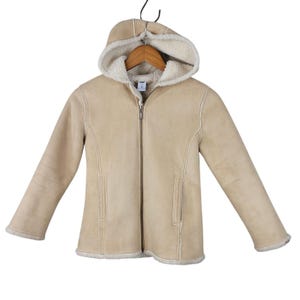 May include: A tan hooded jacket with a full zipper closure. The jacket has a cream-colored, fuzzy lining visible in the hood and along the edges. The jacket is hanging on a wooden hanger.