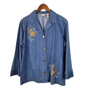 May include: A blue denim jacket with long sleeves and a button-up front. The jacket has embroidered floral designs in shades of yellow, brown, and red.