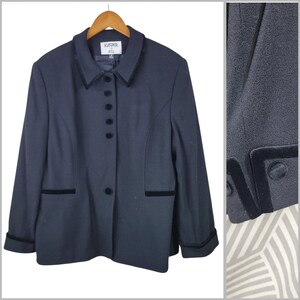 May include: A navy blue blazer with black velvet trim on the collar, pockets, and cuffs. The blazer has a button-up front and is hanging on a wooden hanger. The brand name "Kasper A.S.L." is visible on the label.