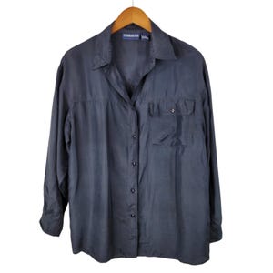 Puede incluir: Una camisa de manga larga en color gris carbón oscuro con cuello clásico y un bolsillo en el pecho. La prenda cuenta con una tapeta frontal de botones oscuros a juego y una etiqueta en el interior del cuello que dice PROLOGUE.