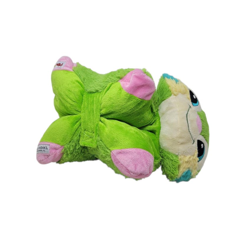 Puede incluir: Un juguete de peluche verde con detalles rosas en los pies y una cara de color claro. El juguete tiene ojos negros y detalles azules y amarillos. El juguete est&aacute; tumbado boca arriba.