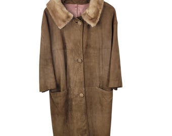 Puede incluir: Un abrigo largo de ante marrón con cuello de piel sintética. El abrigo tiene una botonadura frontal, dos bolsillos delanteros y está colgado de una percha de madera. El abrigo es de estilo vintage.