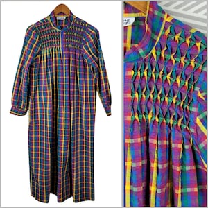 May include: A long-sleeved, ankle-length robe featuring a vibrant plaid pattern in shades of blue, yellow, green, and purple. The garment includes a front zipper closure and intricate smocking detail across the chest and shoulders.