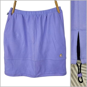 May include: A light purple athletic skirt with an elastic waistband and a small pocket. The skirt has a split on the side and a drawstring with a purple bead. A small logo is visible on the front.