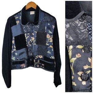 May include: A black velvet jacket with a patchwork design featuring floral, lace, and polka dot patterns. The jacket has a collar and long sleeves.