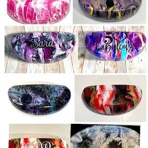 May include: Six different colorful, hand-painted, hard plastic eyeglass cases. The cases feature various abstract designs and glitter. Some cases have personalized text, including "Sara", "50 & Fabulous", and "60 & Fabulous".